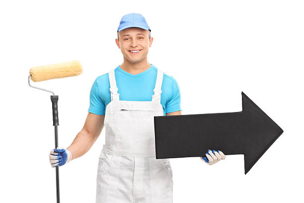 istock Young decorator in a white uniform holding a paint roller 475396058