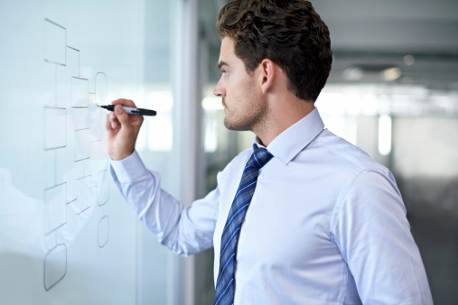 Side view of a businessman drawing a flowchart on a glass wall