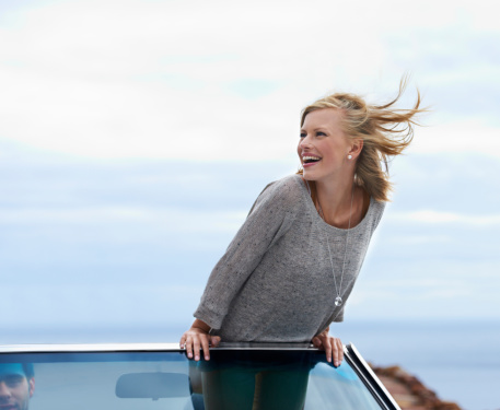 A young woman standing in a convertible and feeling the wind in her hair