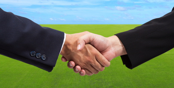 Businessman handshake on green grass field and blue sky