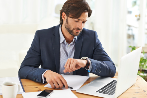 A handsome businessman checking the time on his watch at his desk