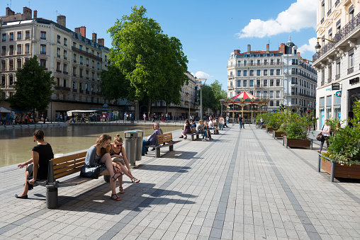 Lyon, France - May 23, 2014: People enjoy an early summer day on benches at a park adjacent to Rue Childebert in Lyon, France. A carrousel is in the distance.