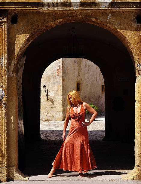 Adult blonde fashion woman in front of big gate in long elegante copper dress