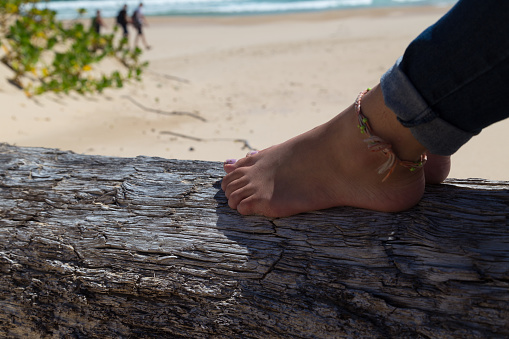 Lady rests her feet on a weatherbeaten tree trunk on the beautiful beach of Robberg peninsula, South Africa