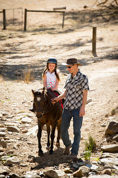 young jockey kid riding pony happy with father horse instructor cute young girl jockey having fun riding pony outdoors happy with Australian American horse instructor in cowboy look teaching ride lesson in summer nature countryside background sports training australia stock pictures, royalty-free photos & images