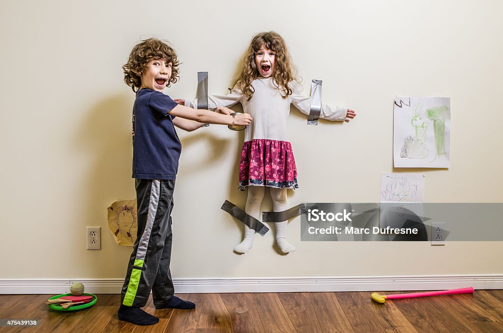 Brother hung her sister on the wall A little boy hung her little sister on the wall using duct tape Child Stock Photo