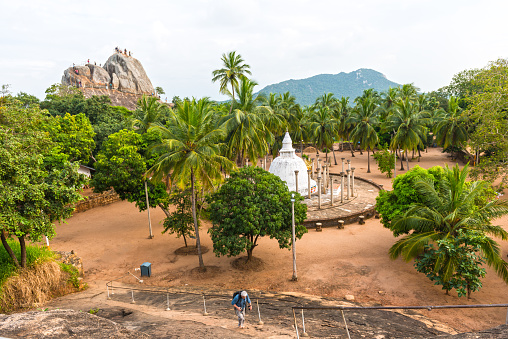 Thuparamaya Dagoba in Anuradhapura - the oldest dagoba on the world. High angle view. Palm trees and in distance holy rock, cliff - Arathana Gala, with small group of people on top. Sri Lanka.