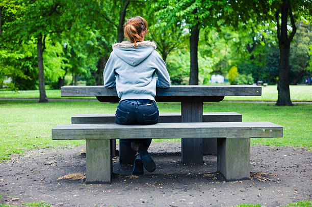 istock Young woman sitting on bench by table in park 475444892
