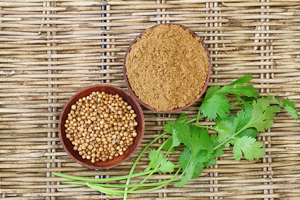 Coriander seeds, powder and leaves on wicker surface