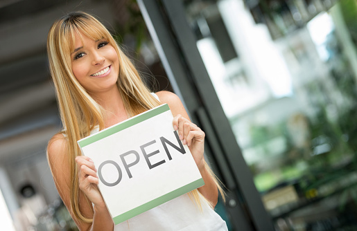 Happy woman working at a restaurant holding an open sign â business owner concepts