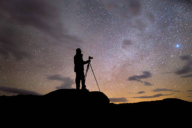 Silhouette of Photographer at Night A photographer taking a photo of the night sky from the top of a mountain. Focus on the stars. astrophotography stock pictures, royalty-free photos & images