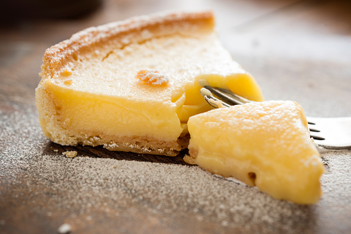 Close up of a Slice of Lemon tart on a rustic wood board, fork slice taking a piece out.