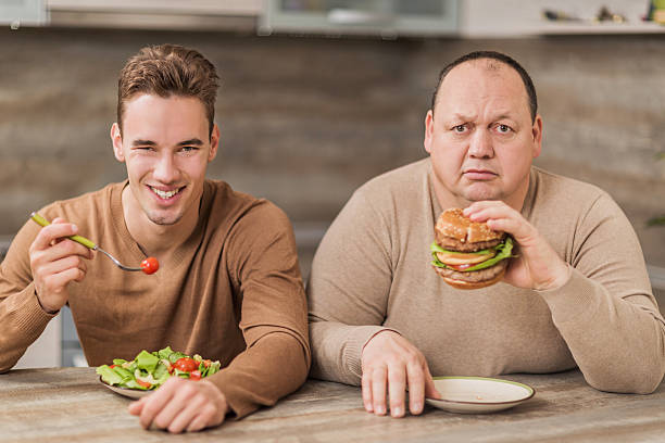 uomo mangia in cucina e guardando la telecamera. - salad vegetable hamburger burger foto e immagini stock