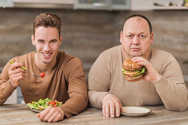 mężczyźni jedzenie w kuchni i patrząc na kamery. - salad vegetable hamburger burger zdjęcia i obrazy z banku zdjęć