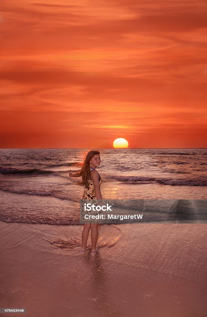 Smiling girl enjoying beautiful sunset at the beach. Smiling child enjoying pretty sunset.  Ocean and  beautiful  red sky with sun in the background. Clearwater beach, Florida. 2015 Stock Photo