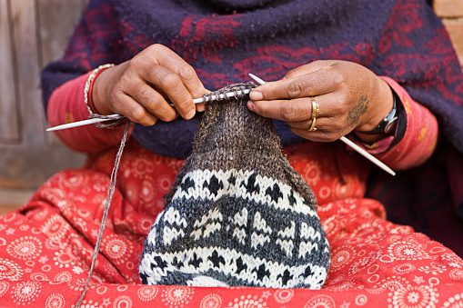 Woman knitting handmade souvenirs and knitted toys on wooden table.