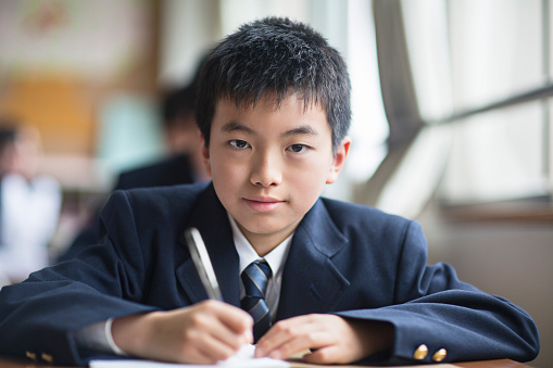 Japanese student boy looking at the camera at the classroom desk.