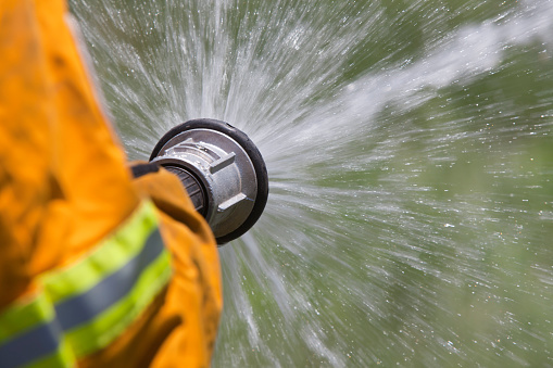 A rural fire fighter wearing high visibility protective clothing with hose spraying water.
