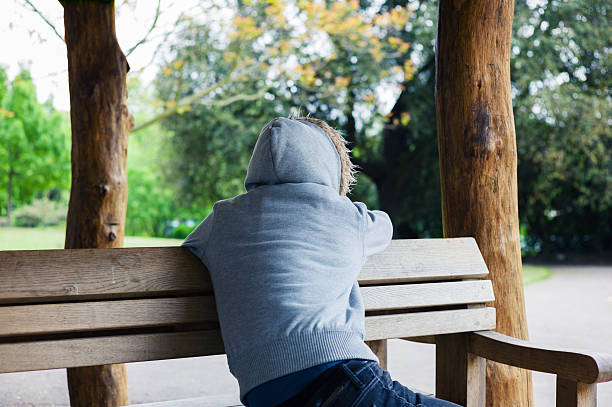 istock Hooded person sitting on park bench 475456456