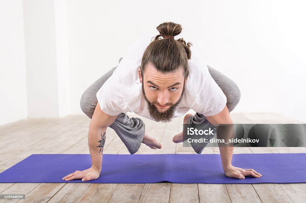 Yoga concept with young man Nice photo of young man practicing yoga. Man meditating on violet fitness mat while doing crow pose. White interior 2015 Stock Photo