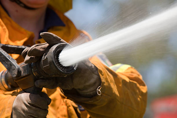 Fire fighter with hose Rural fire fighter in high visibility protective clothing with hose spraying water. fire hose photos stock pictures, royalty-free photos & images