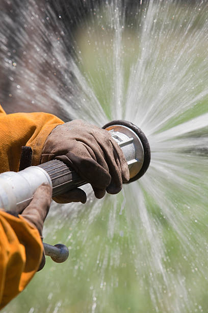 istock Fire fighter holding hose with water spraying out 475471570
