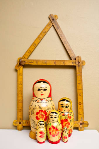 A family of Matryoshka nesting dolls with a folding ruler in the shape of a house behind them