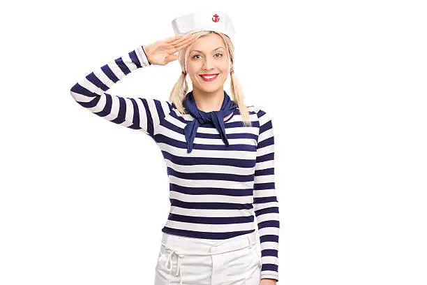Young blond woman in a sailor outfit saluting towards the camera and smiling isolated on white background