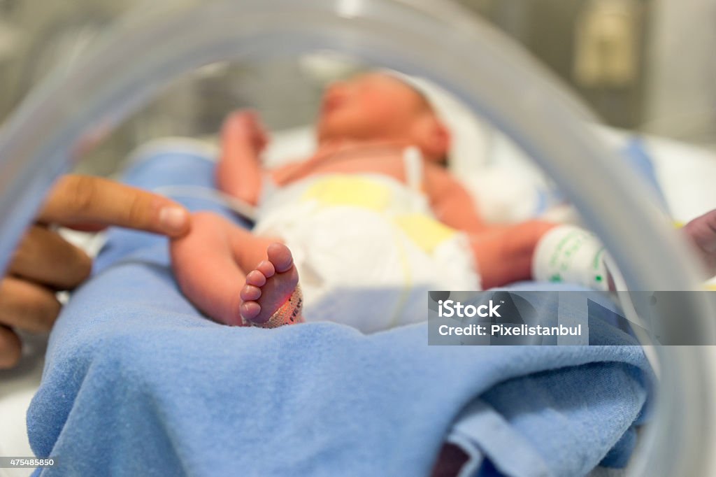 Premature baby and hand of the doctor Photo of a premature baby in incubator. Focus is on his feet and toes. The doctor is touching him to check his reflexes. There are cables and tubes in the out-of-focus area. Premature Stock Photo