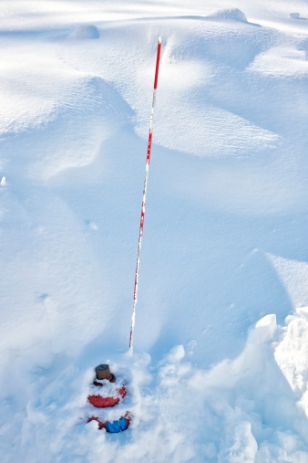 The top of a fire hydrant sticks out of a snowdrift.  The fire hydrant is partially dug out of a snowdrift after a snowstorm.  A winter blizzard has deposited snowdrifts over 6 feet (2 meters) deep.  The red and white pole is used to help find fire hydrant.