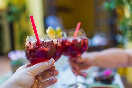 A couple celebrating while clicking two glasses of refreshing sangria with different fruits.