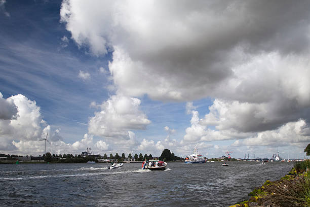Amsterdam, The Netherlands - August 19, 2010: Dutch Coast Guard Ship decked out with flags, followed by multiple smaller boats during the SAIL 2010 boating expo in Amsterdam. Dramatic clouds in the sky.