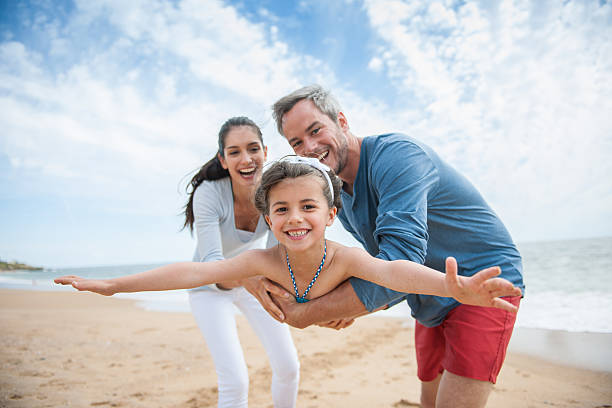 bambina che gioca con la mamma e papà sulla spiaggia - family beach cheerful happiness foto e immagini stock