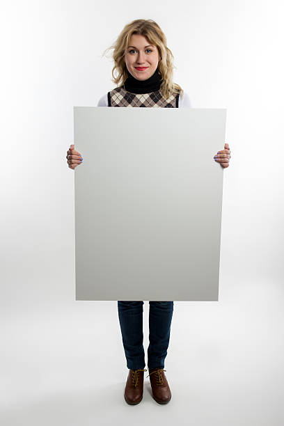 Blond women holds white blank business card, placcard, big white poster, paper, visit card, gift, ticket, pass, present. Portrait of funny handsome nerd guy pulling his suspenders.