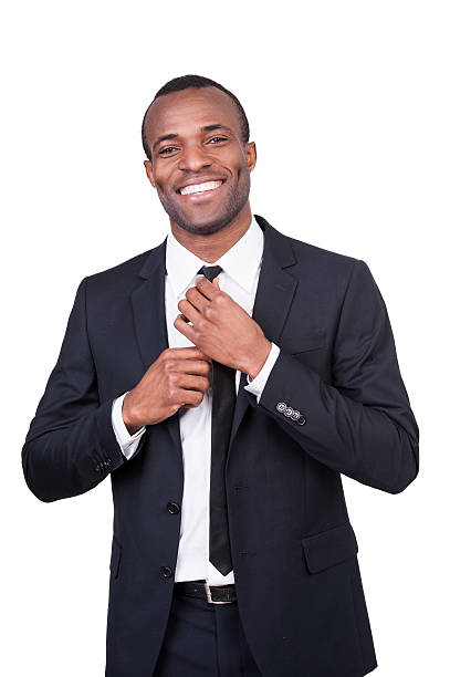 Making business look good. Handsome young African man in full suit adjusting his necktie and smiling while standing isolated on white background man adjusting tie stock pictures, royalty-free photos & images