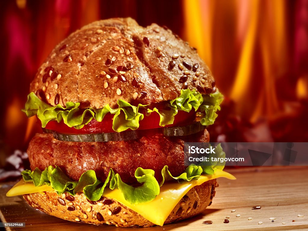 Hamburger with ham on wooden board Double patty hamburger on wooden board on background of fire. 2015 Stock Photo