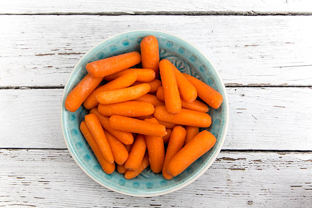 istock Baby carrots in bowl on white wood 475533364