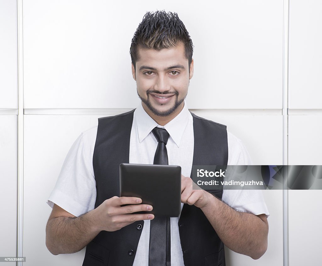 Businessman Young Asian Indian businessman standing on office background and holding a tablet in hands Adult Stock Photo
