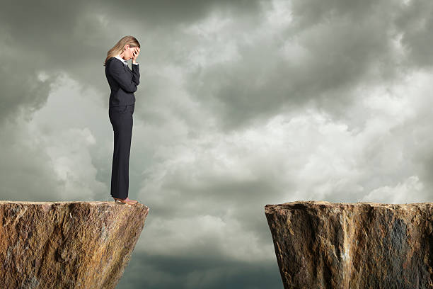Distraught businesswoman standing at the edge of a cliff A distraught businesswoman standing at the edge of a cliff with her head in his hands. She is struggling with the fact that she can't get to the other side. Room for text. ravine stock pictures, royalty-free photos & images