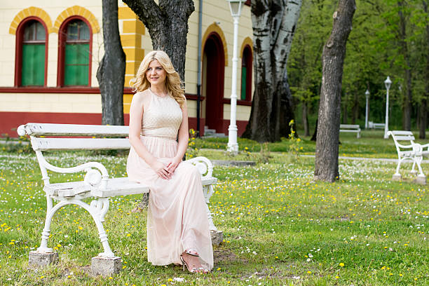 istock Blond woman in evening gown sitting on white bench 475550628