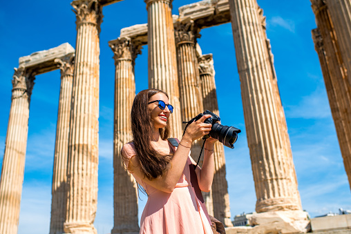 Young and smiling woman photographer taking picture with professional camera of Zeus temple in Acropolis