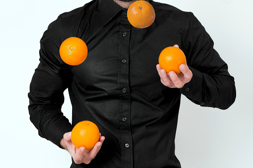 Man in black shirt juggling with four oranges
