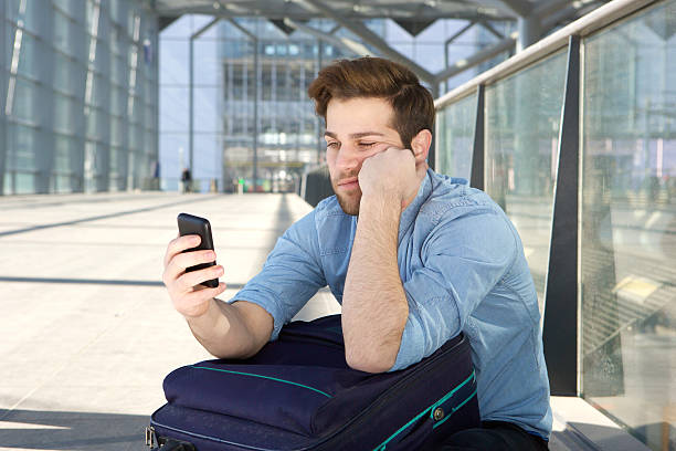 Man waiting at airport with bored expression on face Portrait of a young man waiting at airport with bored expression on face waiting telephone on the phone frustration stock pictures, royalty-free photos & images