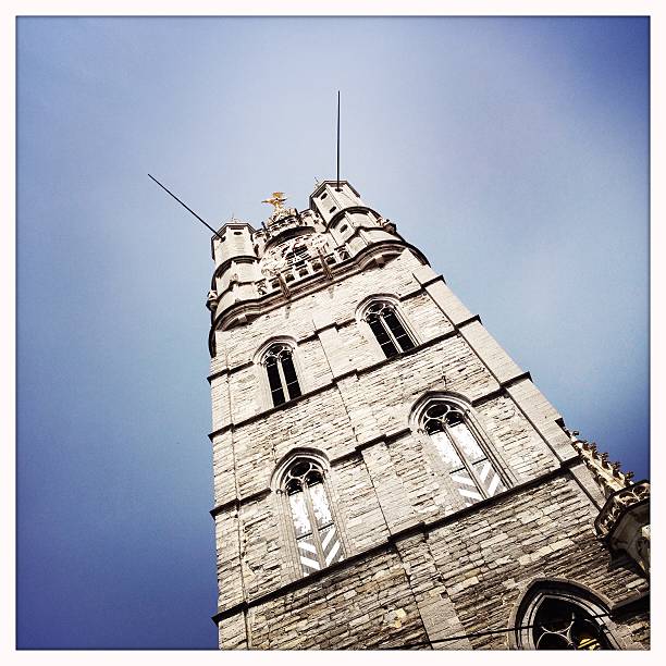 A magnificent church tower rising into the clear blue sky in Bruges. Surrounded by charming brick and white buildings, this tower reflects medieval elegance in a peaceful urban setting.