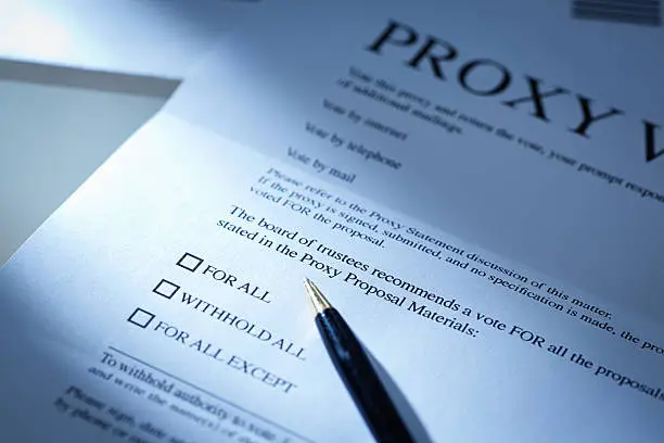 The proxy vote business letter with a pen resting on the document ready to authorize the governing members. Proxy vote by mail, a common business document sent to all participating business interested party and stakeholders. Photographed in horizontal format in dramatic lighting spotlighting the checkboxes.