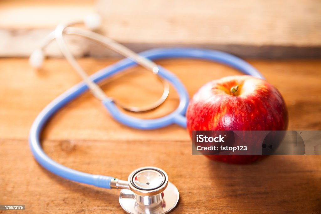 Apple a day keeps the doctor away.  Stethoscope. Red, ripe apple beside doctor's stethoscope. Healthy lifestyle, medical concept. Wooden board background.  2015 Stock Photo