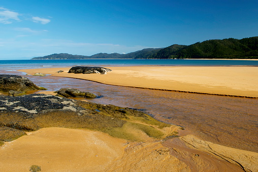 The clear waters and golden sands of Totaranui estuary from a low angle viewpoint as the tide ebbs in.