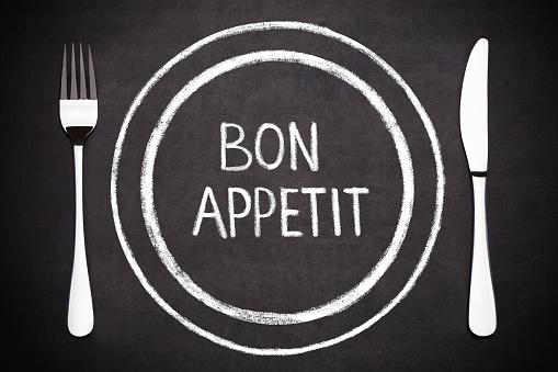 Bon appetit lettering on a plate with a fork and a knife on the side  drawing with chalk on blackboard.