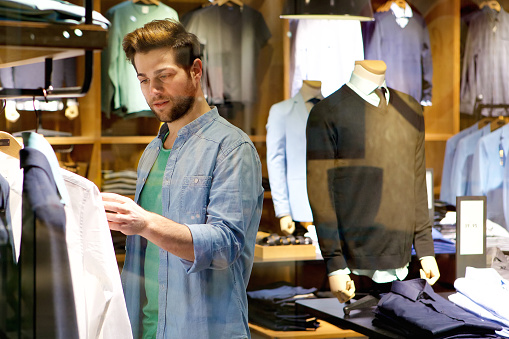 Portrait of a young man looking at clothes to buy at shop