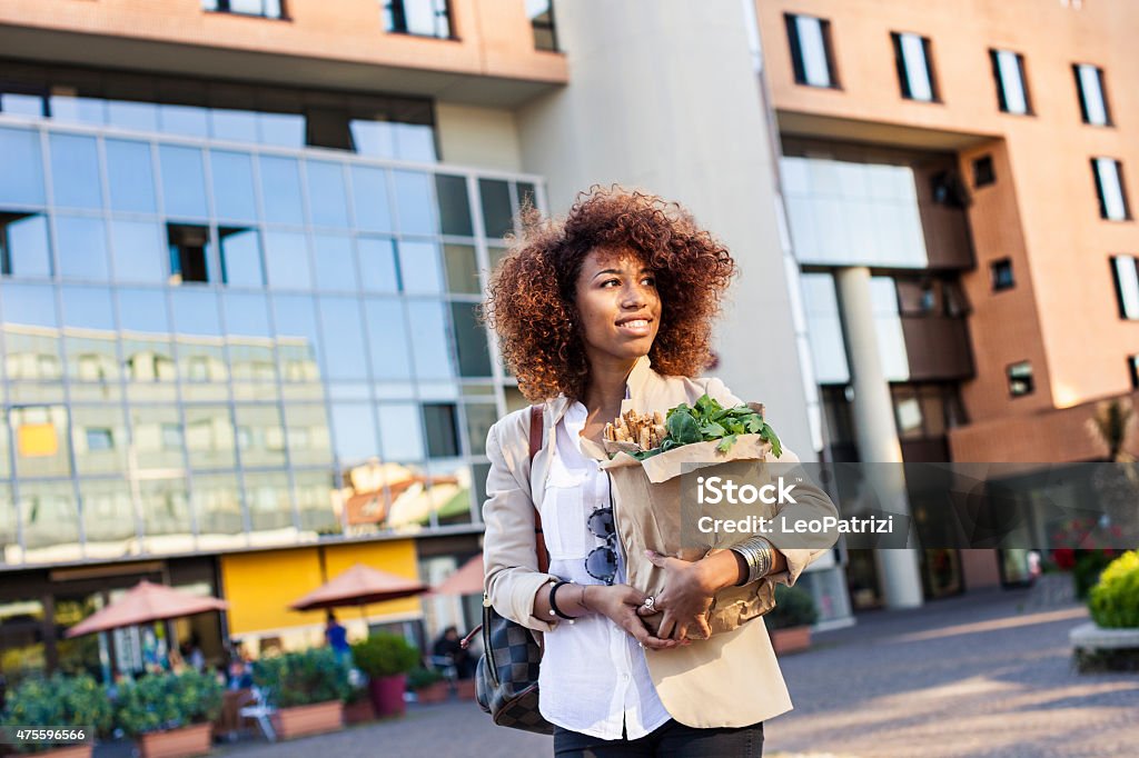 Vegetables and healthy products shopping in the morning Young afro woman holding a shopping bag full of green vegetables and sesame breadsticks walking in the morning before going at work. Groceries Stock Photo